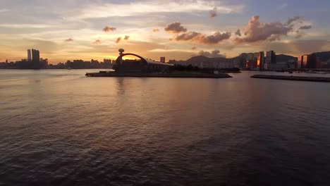 Aerial-footage-or-a-drone-shot-over-a-sea-or-water-in-a-harbor-while-a-city-is-visible-in-the-background-in-silhouette-mode-while-the-sun-is-setting-or-sundown