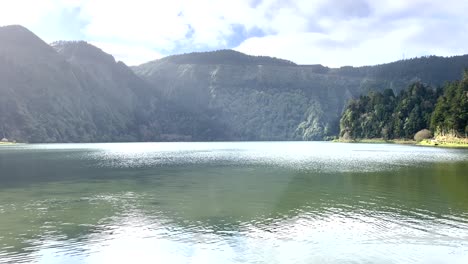 Aerial-video-over-a-very-calm-river-with-light-reflections-on-the-water,-surrounded-by-trees-in-the-Azores,-Portugal