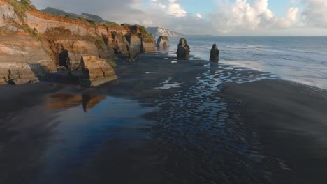 Tourists-Running-Towards-Cliffs-And-Sea-Stacks-On-Coast-Of-Taranaki-At-Three-Sisters-Beach,-North-Island,-New-Zealand