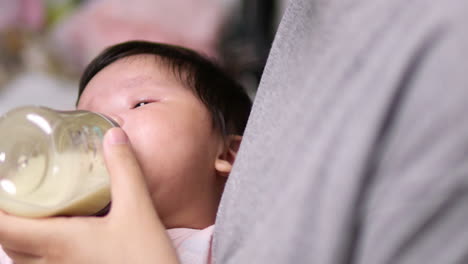 Panning-from-a-blurry-to-a-clear-shot-of-a-baby-who-is-drinking-some-milk-as-she-is-cradled-in-her-mother's-arms