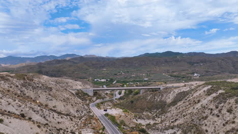 Flight-reverses-from-a-pristine-newly-constructed-rail-bridge-revealing-a-road-below-and-a-vast-rugged-background-landscape-under-a-searing-hot-sky-Sorbas-Almeria-Espana-Spain