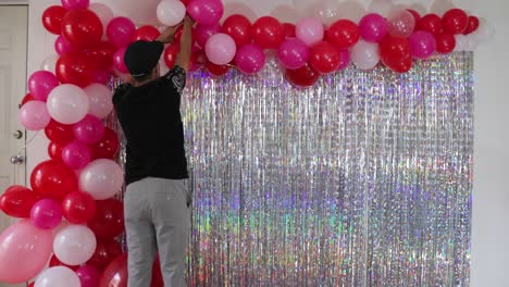 Young-man-decorating-Valentine's-day-wall-with-fringes-and-balloons