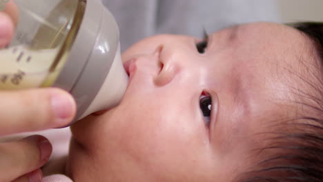 Drinking-some-formula-milk-from-a-baby-feeding-bottle,-a-newborn-child-is-being-lulled-by-its-mother-to-sleep