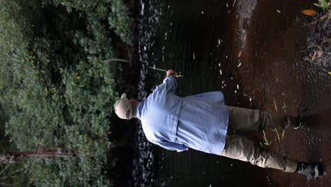 Slow-motion-vertical-footage,-shot-from-behind,-of-a-fly-fisherman-casting-into-a-stream