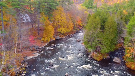 Mont-Tremblant,-Québec,-Canada,-with-a-peaceful-river-flowing-through-a-vibrant-autumn-landscape,-colorful-foliage-lining-the-banks,-and-cozy-houses-nestled-near-the-water's-edge