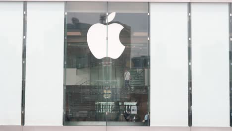 An-exterior-view-of-the-Apple-Store,-showing-customers-ascending-the-staircase,-with-the-company-logo-prominently-displayed