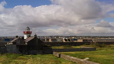 Aerial-orbit-of-Mutton-Island’s-coastline-with-historic-lighthouse-and-rock-walls-across-green-landscape,-rocky-shores,-and-expansive-ocean-in-Galway-Bay,-Ireland-as-flock-of-seagulls-soar-in-sky