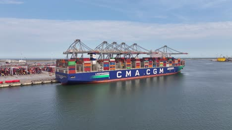 Large-container-ship-docked-at-a-busy-port,-cranes-unloading-colorful-cargo-in-daylight