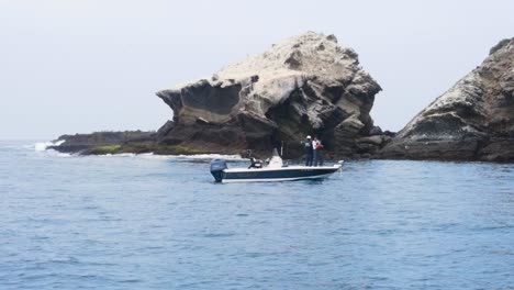 Aerial-orbit-of-a-boat-anchored-in-the-waters-near-the-rocky-coast-of-Coronado-Islands,-Mexico-as-friends-cast-and-fish-off-the-front