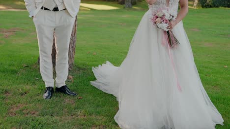 couple-stands-together-on-a-lush-green-lawn,-the-bride-holding-a-pink-bouquet