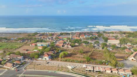 Blue-ocean-and-small-township-on-coastline-of-Indonesia,-aerial-view