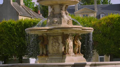 Slow-Motion-Water-Flowing-from-Stone-Fountain-on-Hot-Summer-Day-with-Old-Buildings-in-Background-4K