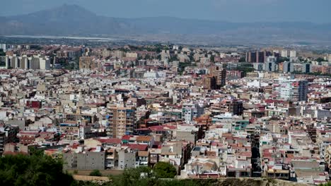 A-panoramic-landscape-of-a-vast-city-highlights-a-mix-of-old-and-modern-buildings,-with-a-majestic-mountain-range-serving-as-a-scenic-backdrop-of-Alicante-city-in-Spain