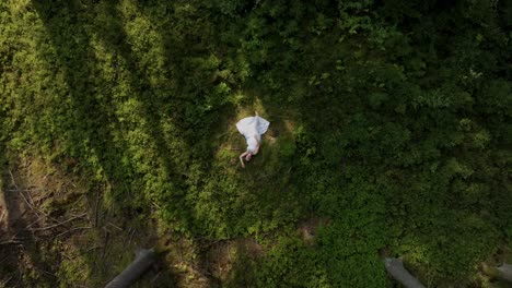 Mujer-Vestida-De-Blanco-Tumbada-En-Un-Bosque,-Vista-Desde-Arriba,-Abrazando-La-Naturaleza-En-Pacífica-Armonía-Y-Relajación.