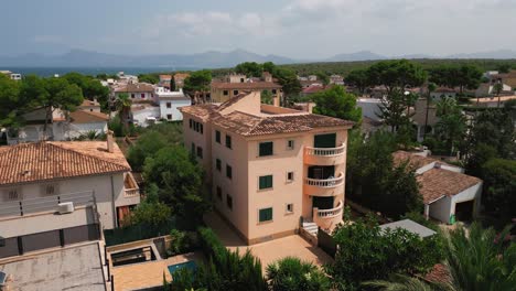 A-drone-shot-highlighting-a-uniquely-styled-block-building-in-Can-Picafort,-Mallorca,-showcasing-its-distinctive-architecture-and-urban-setting