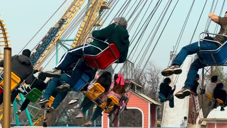 Spinning-chairs-passing-by-full-of-people-establishing-in-the-amusement-park-in-Fantasilandia,-tsunami-attraction-in-the-background