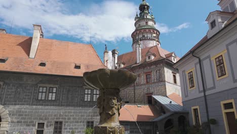 Tilt-up-from-fountain-to-Castle-Tower-in-Český-Krumlov,-Czechia,-overlooking-the-medieval-town-and-surrounding-landscape