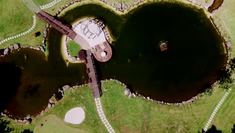 Aerial-view-of-a-large-lake-with-a-bridge-on-a-giant-golf-course-surrounded-by-greenery