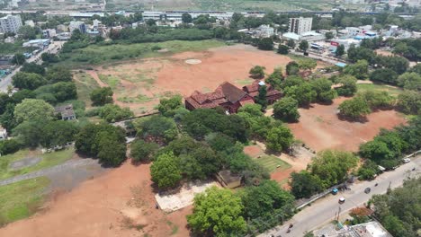 Aerial-Drone-Shot-of-Red-Building-near-Open-ground-with-tree-surrounded-in-the-city