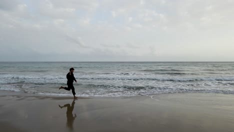 A-lone-man-runs-along-the-beach-in-Calpe,-Spain,-near-the-water's-edge,-creating-a-serene-and-meditative-atmosphere