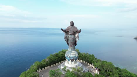 Aerial-view-of-a-large-Jesus-Christ-statue-on-a-hilltop-overlooking-the-ocean-and-greenery