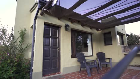 Establishing-shot-of-cozy-outdoor-patio-featuring-two-chairs-under-a-sunshade,-attached-to-a-modern-home-with-a-black-door-and-large-windows