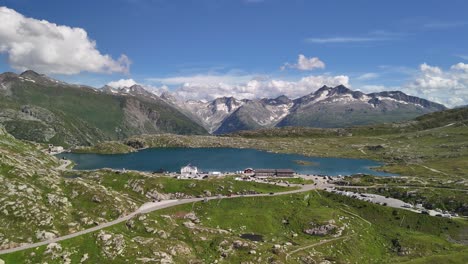 Aerial-view-of-Lake-Totensee-nestled-within-the-mountain-range-in-Obergoms,-Switzerland,-showcasing-the-dramatic-contrast-between-the-serene-lake-and-the-rugged-alpine-terrain