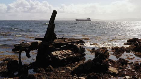 Old-broken-wooden-metal-piece-of-garbage-floats-on-Mutton-Island’s-rocky-shore-with-the-vast-ocean-and-distant-boats-in-Galway-Bay,-Ireland