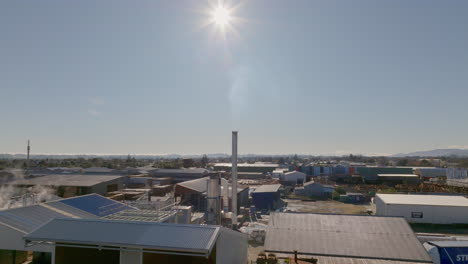 Flying-towards-a-chimney-in-an-industrial-area-on-a-clear,-sunny-day