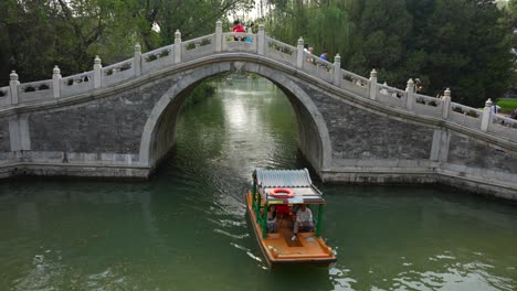 Touristic-boat-navigating-under-Summer-Place-ancient-stone-bridge-in-Beijing,-China