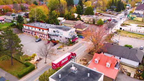 Iconic-red-Coca-Cola-truck-drives-through-small-town-of-Mont-Tremblant-in-Canada,-aerial-view