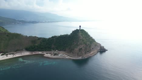 Aerial-view-of-a-large-Jesus-Christ-statue-on-a-hilltop-overlooking-the-ocean-and-greenery