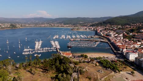 Aerial-view-of-Baiona-Marina-with-boats-docked,-surrounded-by-clear-waters-and-hilly-terrain