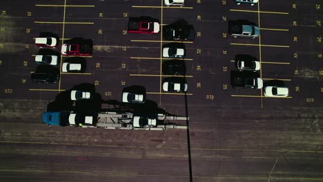 A-car-transport-truck-being-loaded-on-a-huge-parking-lot,-seen-from-above