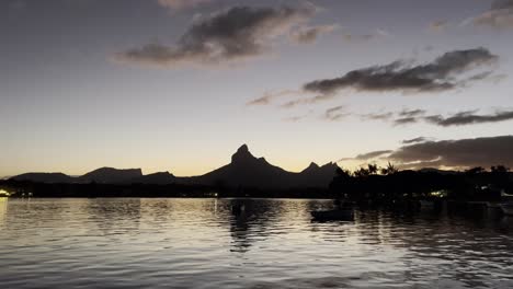 A-calm-and-serene-view-of-the-Rempart-Mountain-early-in-the-morning-from-over-the-water-surface,-passing-local-fishermen's-boats