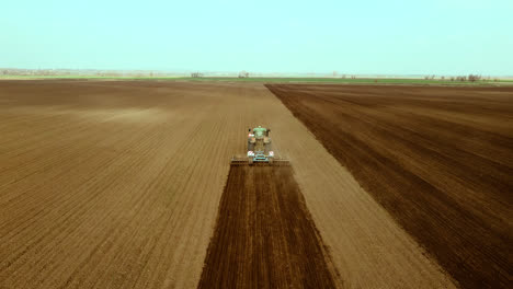 Tractor-processes-large-barren-farmland,-high-angle-shot