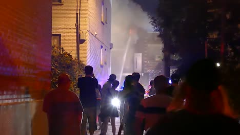 Firefighters-battle-building-fire-as-people-record-scene-on-their-phones-in-downtown-Montreal,-Quebec-at-night