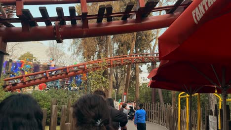 Tilt-down-of-the-Tren-Minero-ride-with-a-group-of-people-walking-under-the-rails-at-the-Fantasilandia-amusement-park,-Santiago,-Chile