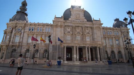 The-Palacio-Consistorial-stands-proudly-with-Spanish-flags-waving-in-the-air,-accentuating-the-building’s-historic-charm-and-symbolizing-national-pride-against-a-majestic-backdrop