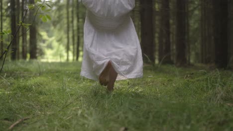 Woman-with-bare-feet-is-walking-in-the-green-grass-in-the-forest-on-a-sunny-day