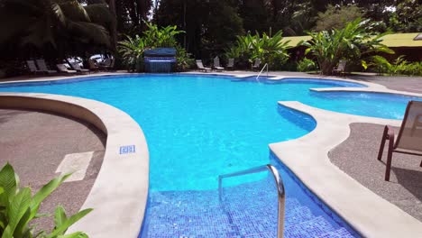 Charming-empty-outdoor-blue-colored-pool-with-fresh-water,-jacuzzi-area-and-waterfall-in-a-tropical-exotic-garden-on-a-sunny-day-in-Tortuguero,-Costa-Rica