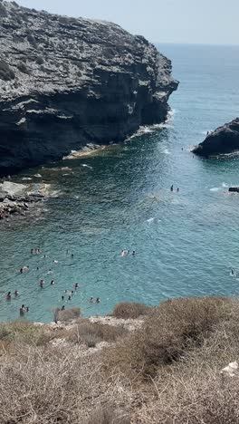 People-at-the-hidden-small-beach-in-La-Manga,-Murcia,-enjoying-the-coolness-of-the-water-during-the-hot-summertime