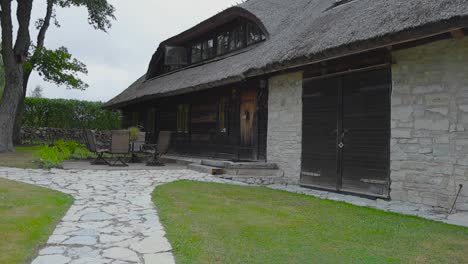 Old-restored-limestone-traditional-building-in-Saaremaa-Estonia-that-has-a-straw-or-rye-roofing-surrounded-by-limestone-roads-and-a-beautiful-garden-with-short-green-mowed-lawn-and-grass