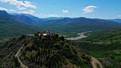 Impresionante-Paisaje-Griego:-Una-Pequeña-Capilla-Blanca-Situada-En-Lo-Alto-De-Una-Colina-Con-Vistas-A-Un-Exuberante-Valle-Verde.