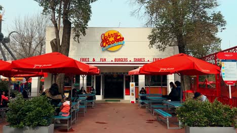 Panoramic-establishing-of-people-walking-past-the-Johnny-Rockets-thematic-hamburger-restaurant-on-a-sunny-day,-Santiago,-Chile