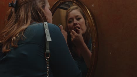 Woman-looking-in-a-mirror-and-putting-on-lipstick