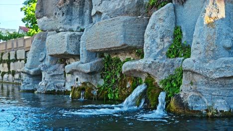 Las-Intrincadas-Tallas-De-Piedra-De-Un-Antiguo-Santuario-De-Agua,-Donde-Arroyos-Claros-Fluyen-Suavemente-Desde-Las-Bocas-De-Figuras-Sagradas.