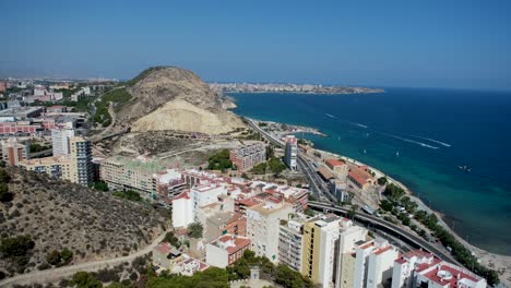 A-sweeping-aerial-view-captures-a-city-nestled-along-the-ocean-shore,-blending-urban-structures-with-the-natural-beauty-of-the-coastline-and-blue-waters