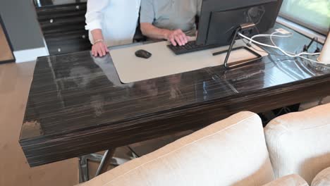 older-couple-sit-behind-their-computer-desk-and-give-the-thumbs-up-sign-and-smile