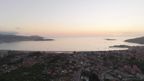 aerial---Nigrán-and-Playa-América-during-sunset,-calm-waters,-and-village-below